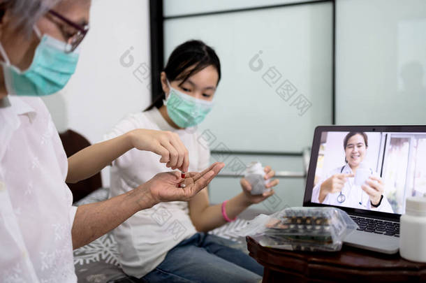 亚洲老年妇女正在根据女医生的建议在视频会议上吃药，生病的老年人在视频电话上使用笔记本电脑聊天，询问有关疾病和流感药物的情况，并进行在线咨询