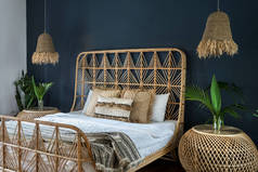 波希米亚风格的室内舒适的房子与少数民族装饰。精致的卧室，床头柜上方点着灯，舒适的床上有枕头，有仙人掌植物，还有深蓝色墙壁上的空间