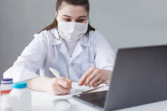 戴面具坐在办公桌前的欧洲容貌医生的女人，在笔记本电脑后面工作