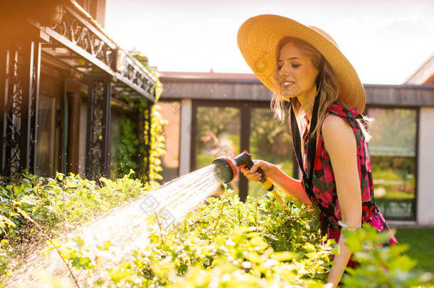 夏天，戴着帽子的漂亮微笑的女孩，在<strong>花园</strong>里浇灌着<strong>花园</strong>的软管，为博客或<strong>广告</strong>拍照