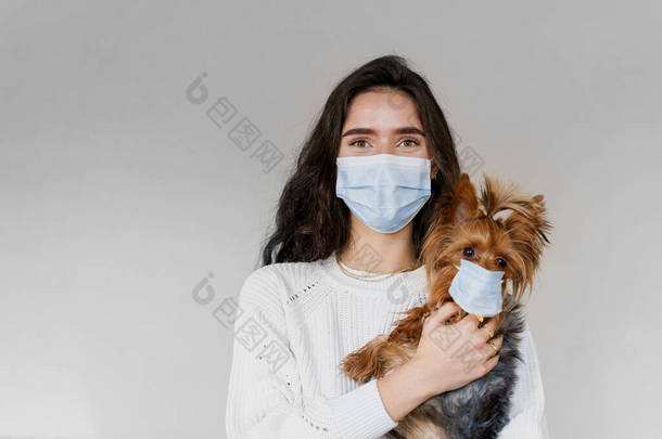 年轻迷人的女人与狗约克郡宠物狗，都戴着保护面具的白色背景。近照。隔离。预防措施。保健和宠物护理。人和宠物