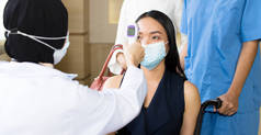 亚洲妇女在医院接受体温测试以测量体温，而她却必须一直戴面具.