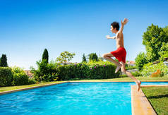 一个英俊的男孩从半空中跳到游泳池的水景中，手举起来