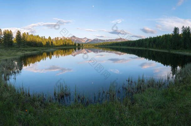 一座长满青草的高山湖上的全景。雪山、云和<strong>月亮</strong>在<strong>水中</strong>反射出来.夏夜，阿尔泰.