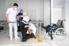 理疗师帮助白种人残疾老人在康复中心带着双杠行走. 