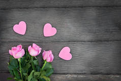 木制背景上有红心的玫瑰。粉红色心形的粉红花朵，有复制空间，深色木制背景