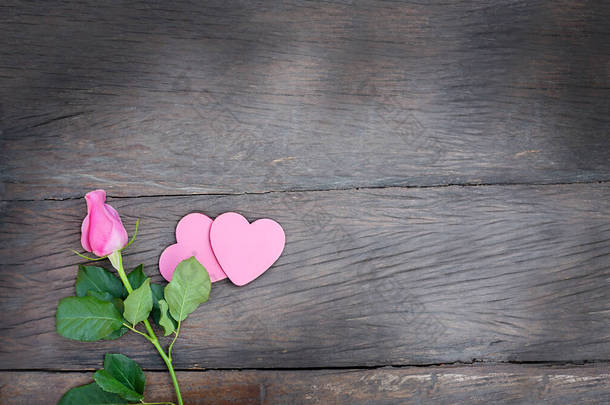 在木制的背景上带着一对夫妇的心站了起来。粉色心型粉红花，叶面为深色木制背景