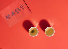 两杯中式茶杯，红面上有红茶和水蒸气。用粤语写上新年快乐字样的红包.