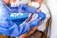 戴口罩的老人穿着防护服看着他，眼镜蛇面具给他注射了验尸疫苗