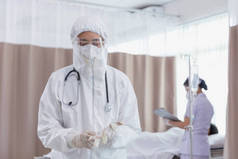 身穿COVID防护服的医生正在摘取手套。医生们戴着COVID-19防护手套，在国家检疫控制区对病人进行检查和治疗.