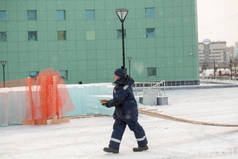 一位身穿蓝色夹克、手拿着木板头罩的建筑工人沿着建筑工地走着