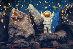 Astronaut standing on rocky mountain celebrating with raising arms while falling shiny golden confet