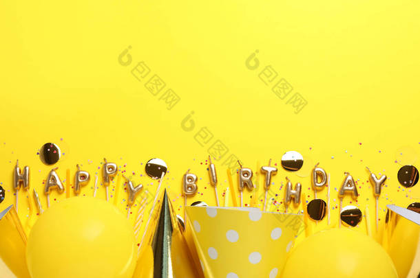 Phrase Happy Birthday of candles and party decor on yellow background, flat lay. Space for text