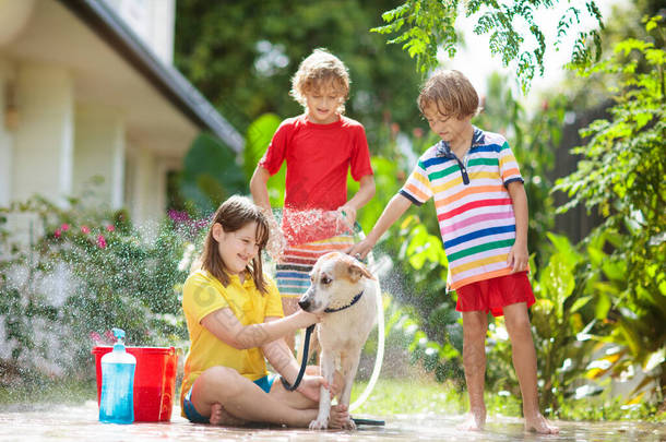 孩子们在夏天的花园里洗狗.水管和洒水的乐趣为孩子。百花盛开的<strong>后院</strong>,孩子们在户外的庭院里洗小狗.孩子们玩。带着宠物的孩子家庭浴犬。动物护理.