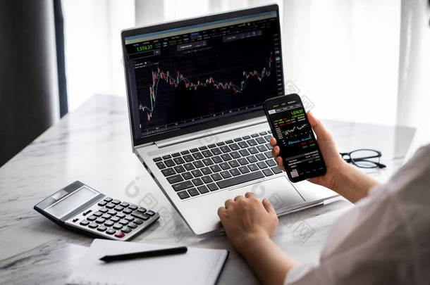 手持智能手机与股票市场数据并用笔记本电脑显示图和图表进行分析。网上投资概念