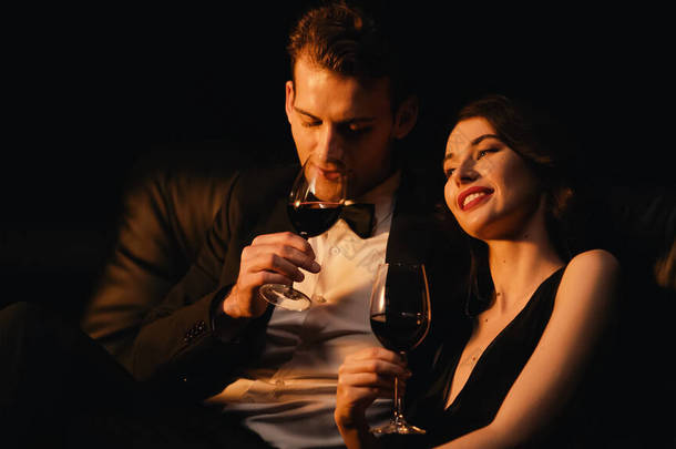 年轻貌美的夫妻举杯红葡萄酒隔离在黑色中