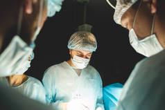 一个由外科医生、助理和麻醉师组成的国际专业小组对全麻病人进行复杂的手术。低调的黑暗大气摄影主题.