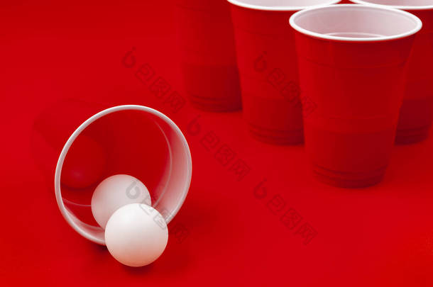 红色背景下的杯和塑料球。啤酒乒乓球比赛