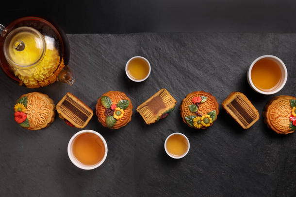 五彩缤纷的月饼中国中秋节装饰在黑色石板背景的小白瓷茶壶上