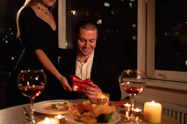 情人节那天晚上，一个女孩用蜡烛送礼物给一个男人晚餐，两人共进晚餐，一个装有惊喜礼物的盒子。情人节庆祝的概念。<strong>横向</strong>射击.