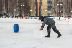一位穿着冬季工作服的工人在一座冰镇的建筑工地上推挤一块冰块