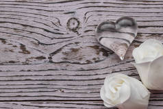 Two white rose buds and a glass heart on a wooden background. The concept of Valentine's Day. Flat l