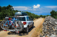Roadcar 与 roofbox 和自行车在橄榄树上地中海尔岛在克罗地亚在克罗地亚地中海尔岛上的橄榄园里的道路上