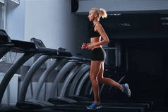 年轻漂亮的竞技女人在健身房的跑步机上