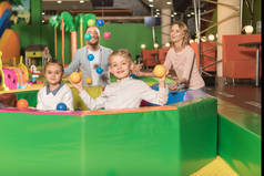 快乐的父母看着可爱的小孩子在镜头里微笑, 玩游戏中心的五颜六色的球