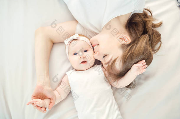 一个快乐的母亲亲吻婴儿躺在床上的<strong>最高</strong>视图.