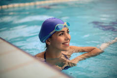 美丽的年轻女子微笑着在游泳池边上戴着游泳帽和护目镜.