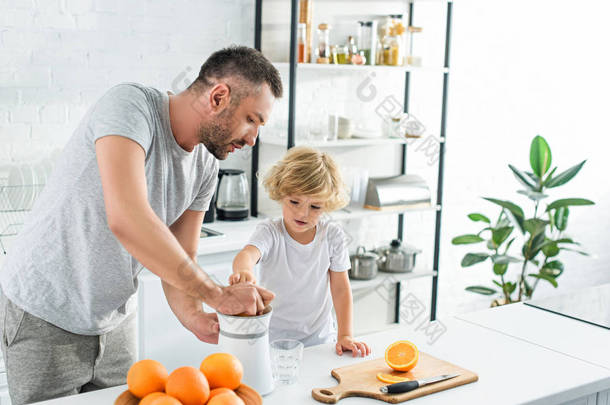 父亲和小儿子挤压在厨房的儿子桌上做新鲜橙汁 