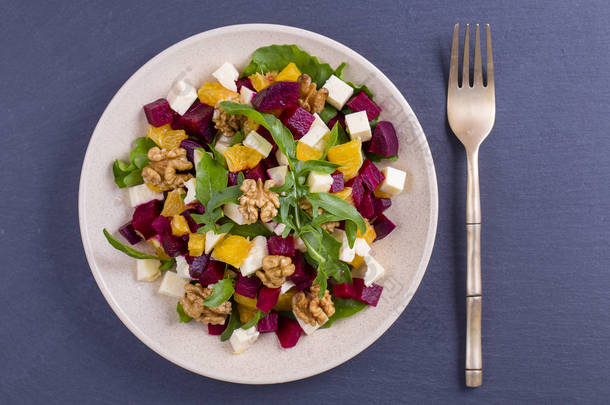 健康素食沙拉与甜菜根, 绿色芝麻菜, 橙色, 羊乳酪和核桃在白色板材, 关闭, 顶部视图