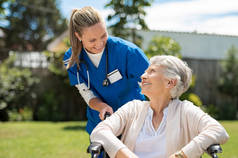 护士照顾在轮椅室外的老太太。友好的医生照顾在轮椅上的老年残疾妇女。快乐的老年妇女与她的照顾者在护理家庭公园.