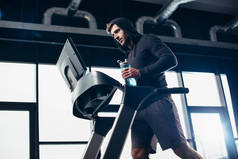 在跑步机上锻炼头套、在健身房用水盛放运动瓶的帅气运动员的低角度视角