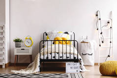 黄色针织枕头在单金属床与图案羽绒被和白色温暖的毯子在宽敞的卧室内部与复制空间在空的白色墙壁