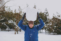 微笑的年轻人穿着蓝色的冬天温暖的衣服, 在雪园或户外的森林里, 头上拿着大雪球玩耍。冬季的乐趣, 休闲的假期。爱情关系家庭人的生活方式概念