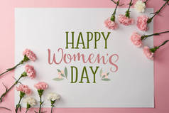 top view of pink and white carnation flowers and greeting card with happy womens day lettering on pi