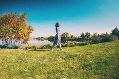 瘦小的女孩走在河边。一个穿着衣服的女人在绿草上散步。褐发女郎在公园里休息.