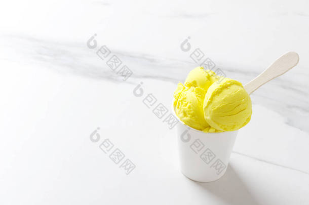 美味的柠檬冰淇淋在纸杯上的白色桌子。阳光明媚的夏日和美味的小吃