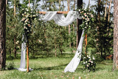 婚礼拱门的盛开装饰与玫瑰，康乃馨和紫杉树。美丽的户外婚礼。白色和粉红色。婚礼照片区。花卉概念。婚礼详情