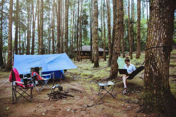 亚洲妇女旅行自然放松。坐在使用笔记本工作。在吊床上。位于清迈国家公园多伊·艾塔农的露营地。在泰国