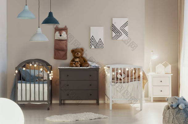 一个柔和的卧室内部与木制婴儿床，米色墙壁和可爱的泰迪熊在一个灰色的抽屉箱的真实照片