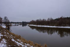 在多云的天气里，有河流的冬季风景，河岸上有反光和雪