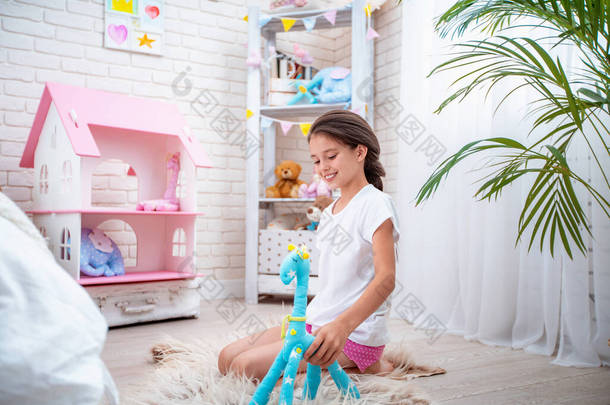 穿着轻便睡衣快乐可爱的女孩，穿着毛织物做的长颈鹿玩具在孩子们的房间里玩耍。房间里充满了灯光和玩具。<strong>迷人</strong>的女孩快乐而漫不经心地微笑和玩耍.