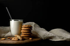 燕麦饼干，一个曲奇饼坏了，杏仁坚果。杯子里的牛奶，有双层墙壁和玻璃管。在切割板和白色纺织品。静谧的生活