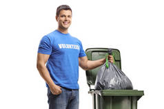 年轻男子自愿地把一个塑料袋扔进一个被白色背景隔开的垃圾桶