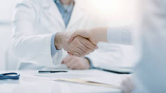 医生和病人在办公室握手，他们坐在办公桌前，手拉手