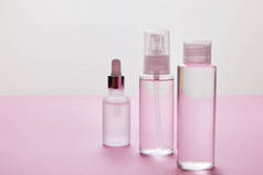 粉色和灰色背景的喷雾、化妆品瓶和装有液体的血清瓶  