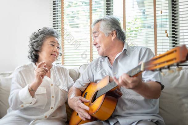 浪漫的亚洲资深夫妇一起唱和弹吉他。快乐的微笑老年吉他手男人和老声乐女人享受着他们的<strong>退休</strong>生活。生活方式、乐器、派对.